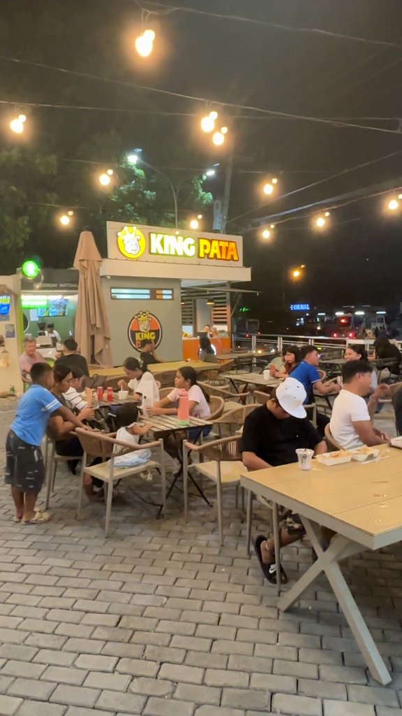 屋台エリアの屋外席。電球のライトの下に木のテーブルが並び、奥にKING PATAの屋台