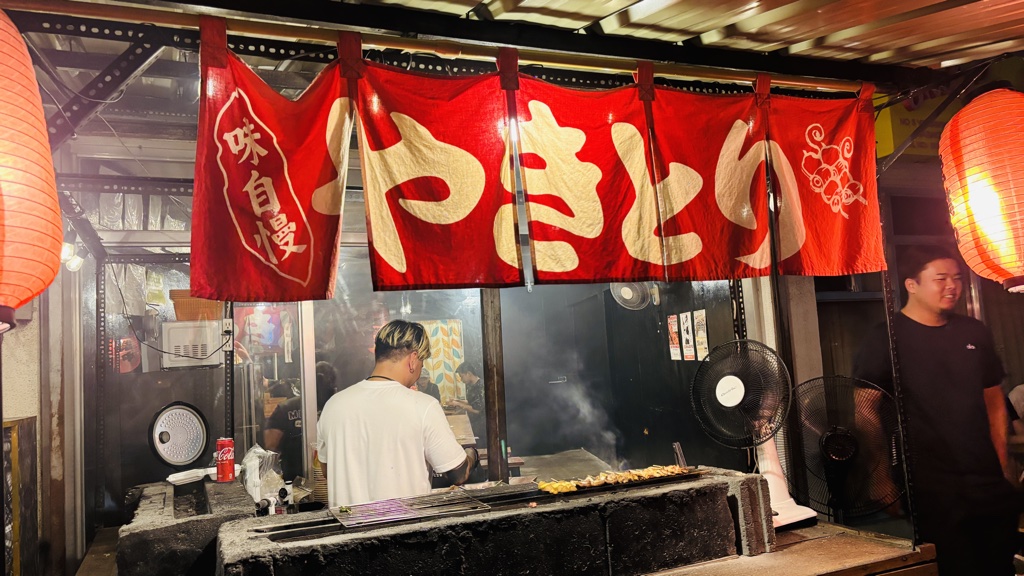 赤いのれんに大きく「やきとり」の文字。のれんの奥で串を焼くスタッフ