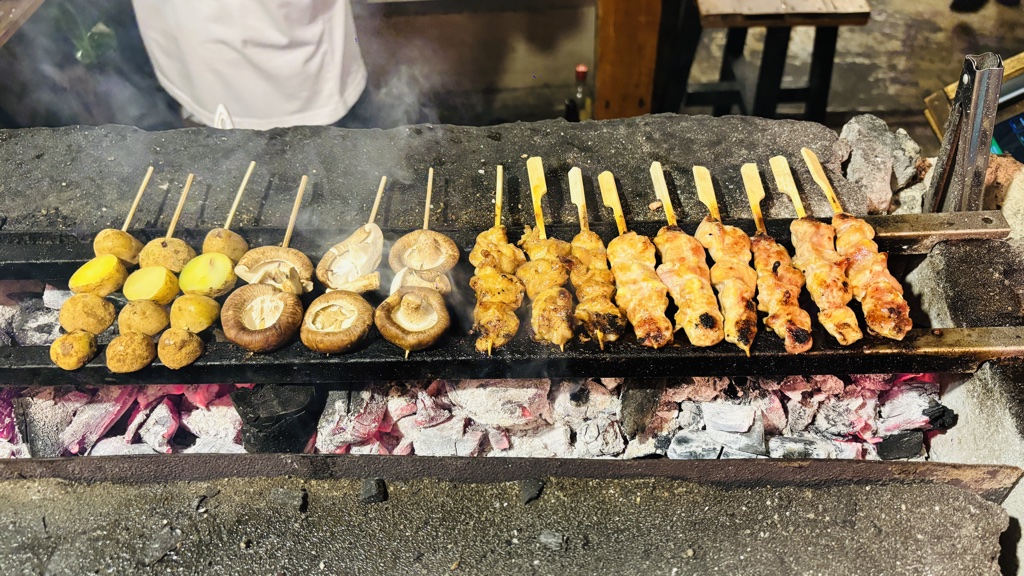 炭火の焼き台。白くなった炭の上に、じゃがいも・しいたけ・鶏肉の串が並ぶ