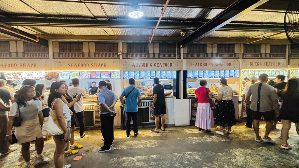 「SEAFOOD SHACK」の看板が並ぶシーフード屋台と、注文する地元の人たち