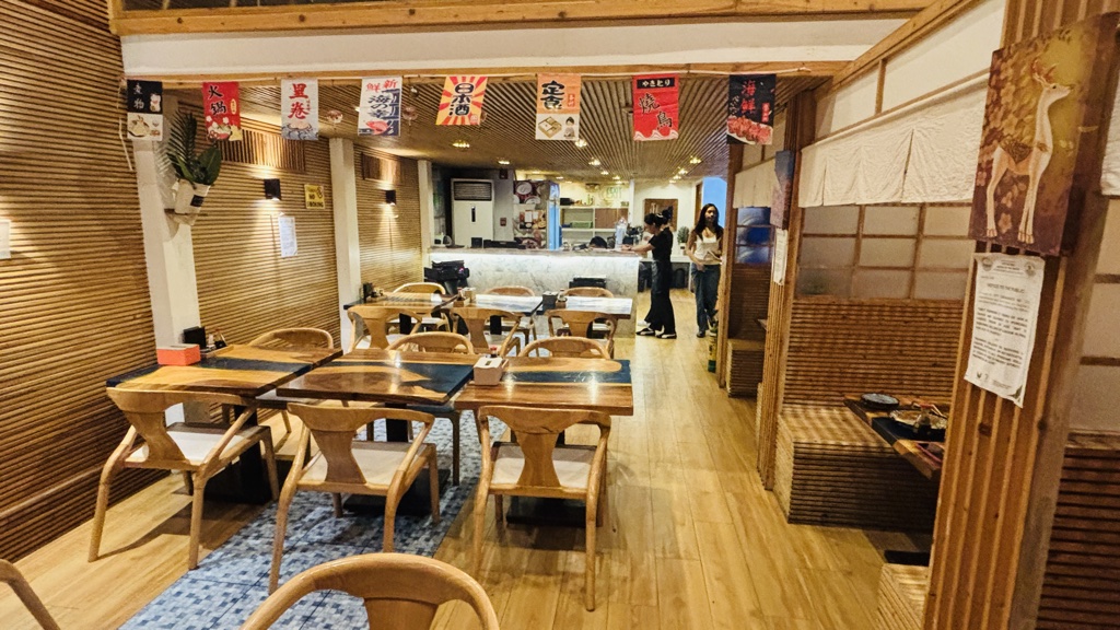 利久（Re-Q）の1階の店内。木の壁と木のテーブル席、天井から下がる日本語の旗、右側に仕切りのある席