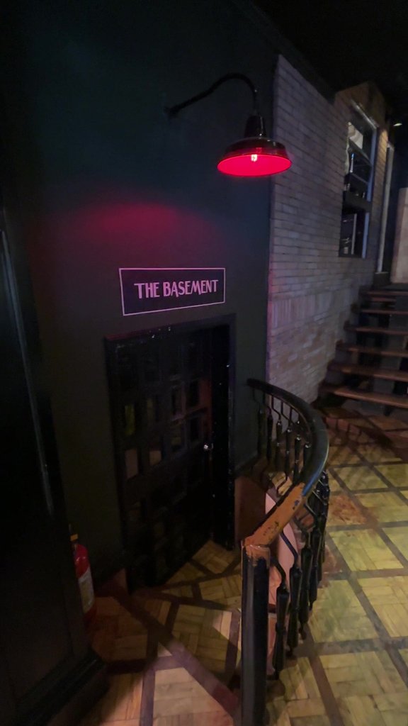 赤いランプに照らされたTHE BASEMENTの看板と、地下へ下りる階段